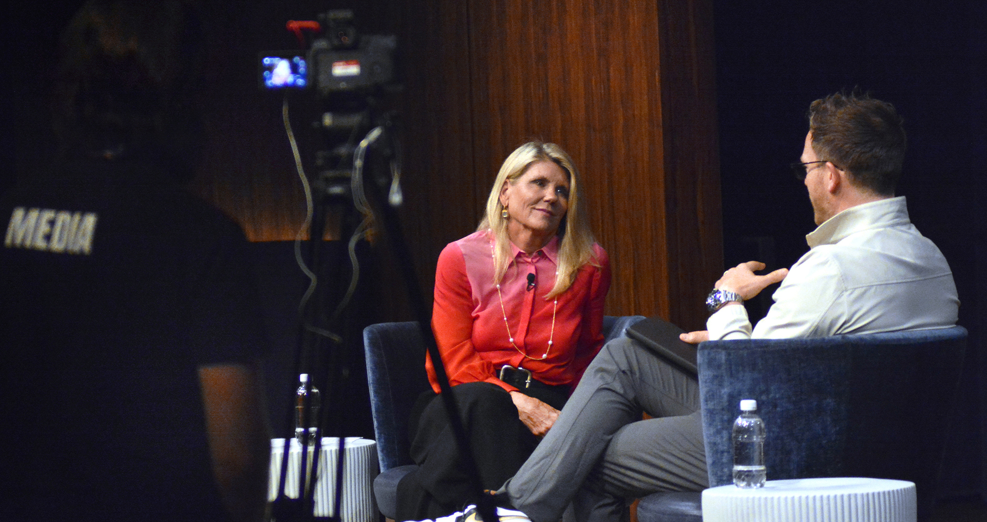Kathy Ramsberger speaks with Ken Pozek on a stage under spotlights.